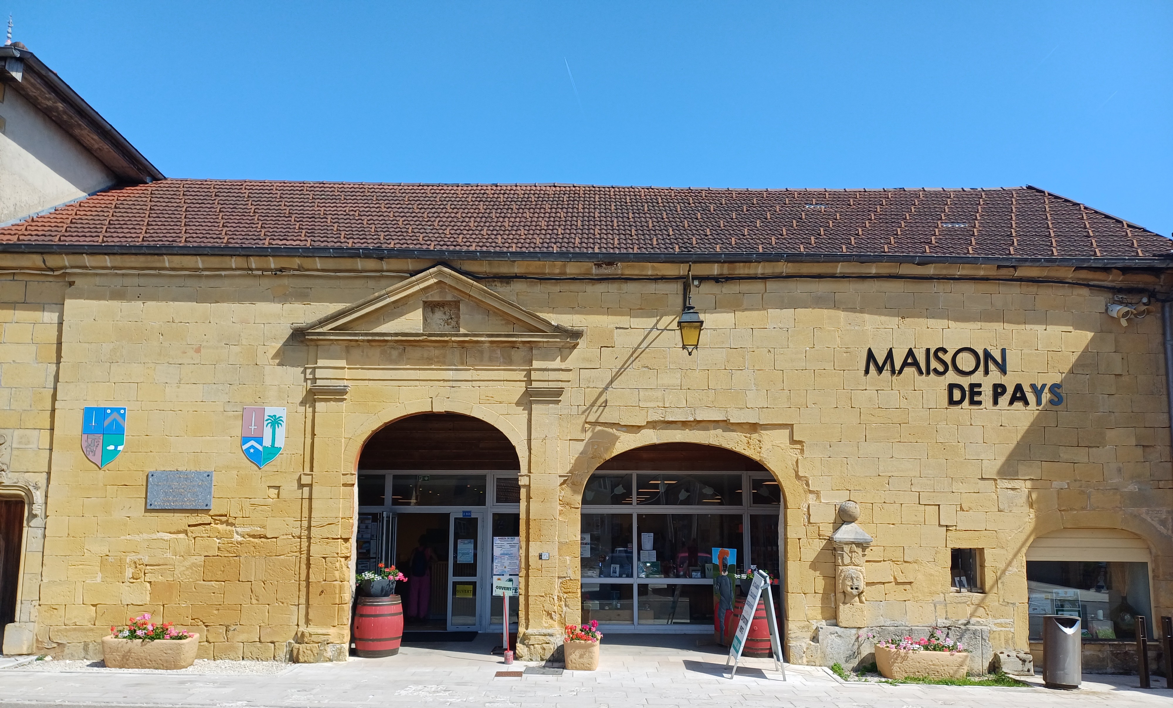Façade en pierre de la Maison de Pays de Nozeroy, ancienne halle avec ses arcades, sous un grand ciel bleu